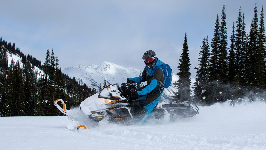 Snowmobiler turning in the snow with mountains in the background