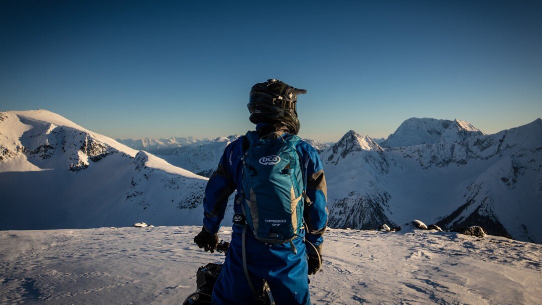 Un motoneigiste contemplant la vue au sommet d'une montagne