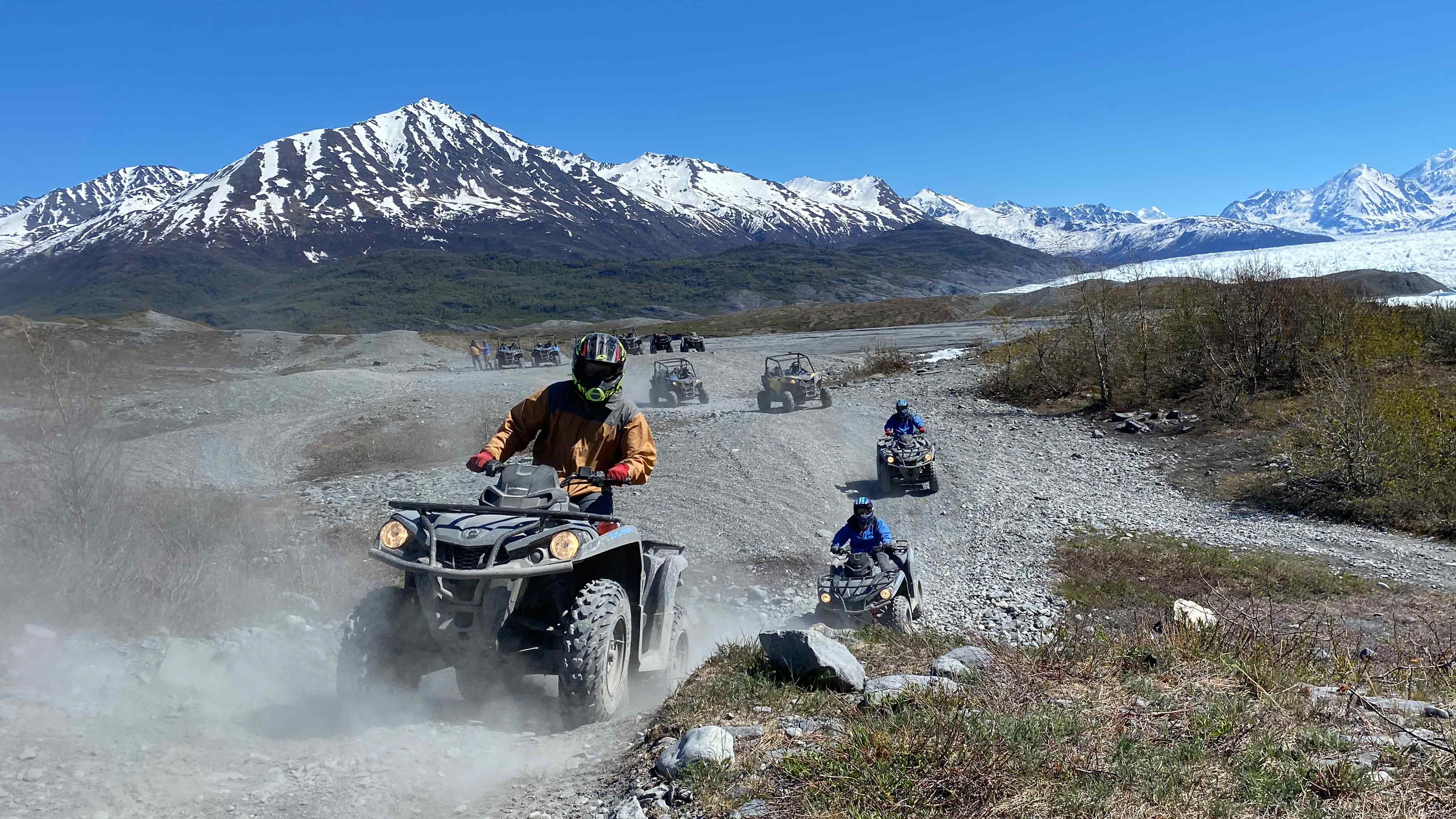 People ride off-road vehicles beneath snowcapped mountains