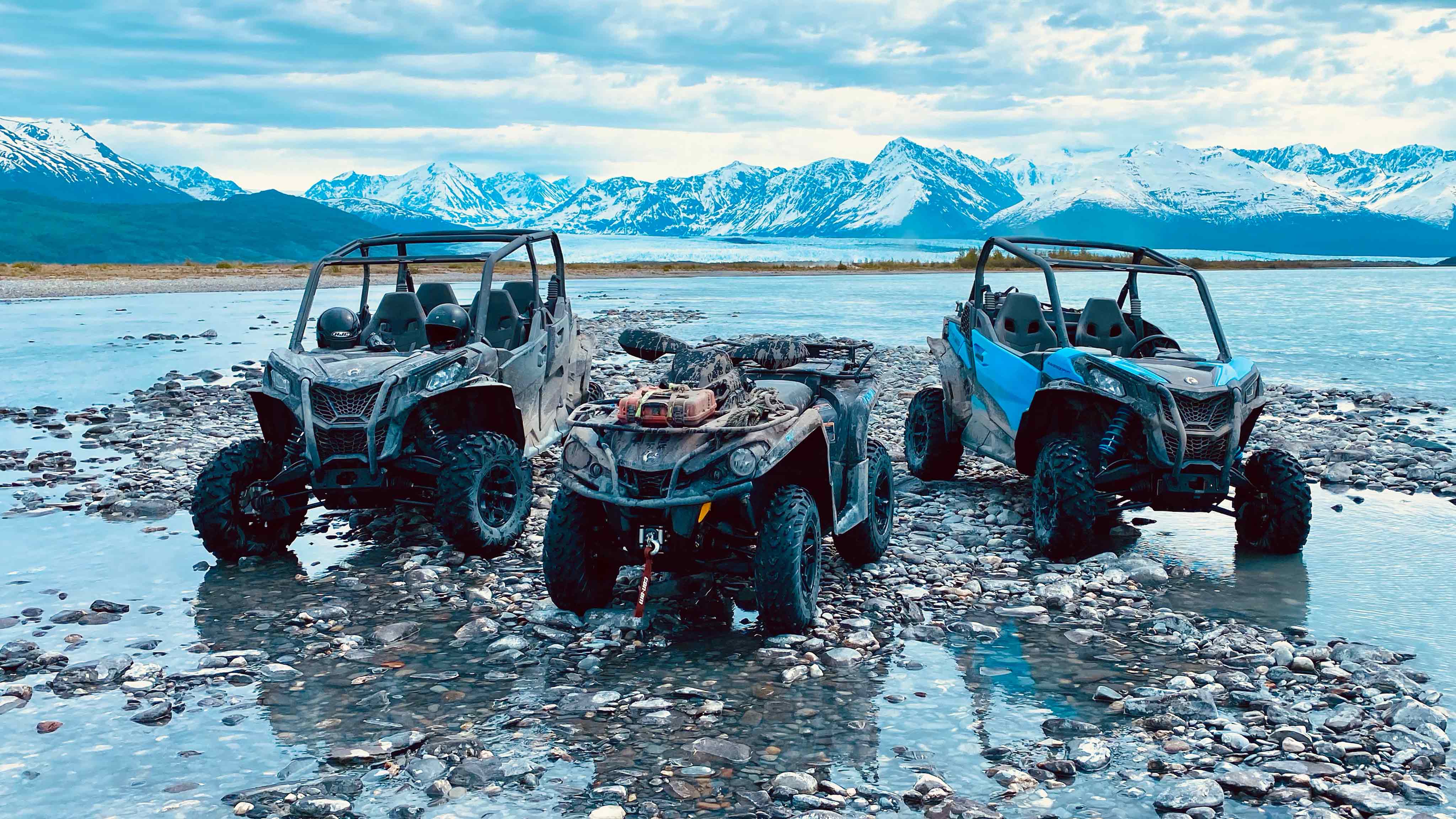 Two SxSs and ATV parked on rocky shore