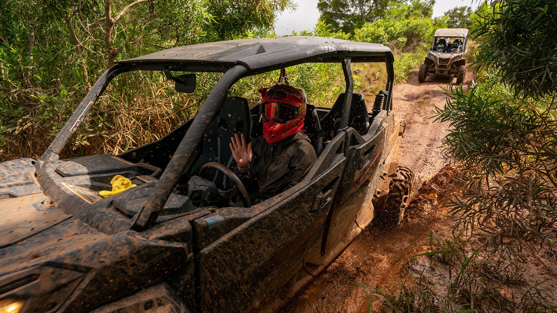A rider waving inside a muddy vehicle