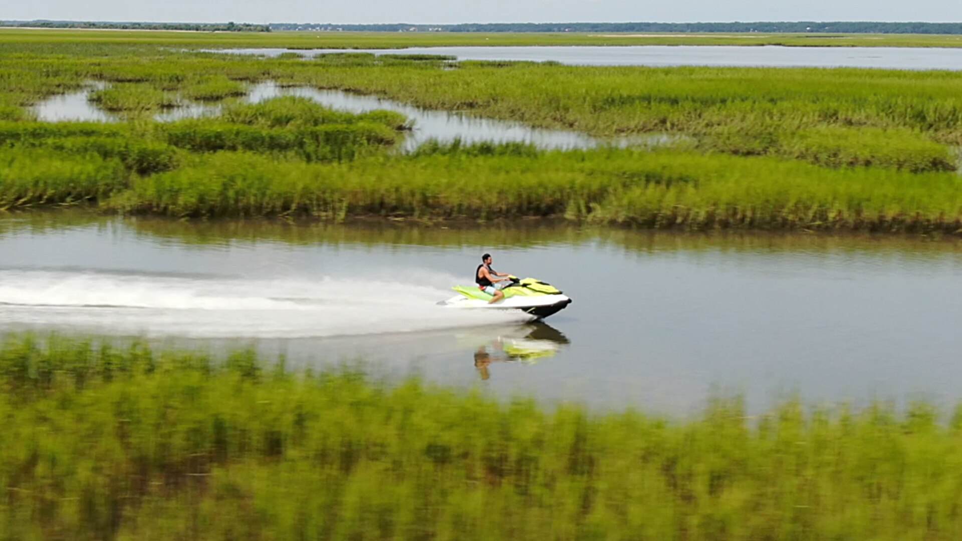 A man riding a Sea-Doo near water plants