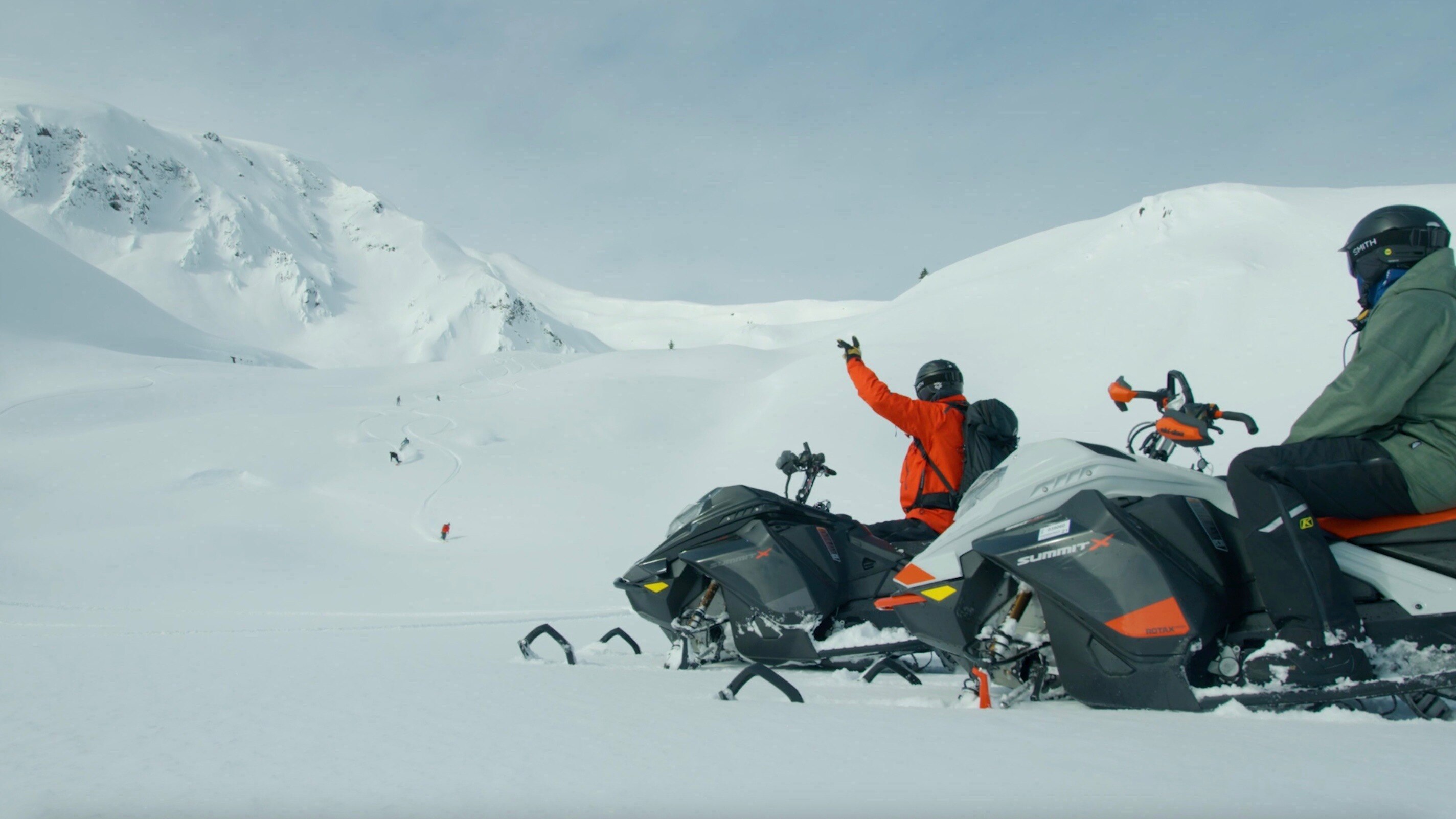 Two snowmobilers waiting at the bottom of a mountain