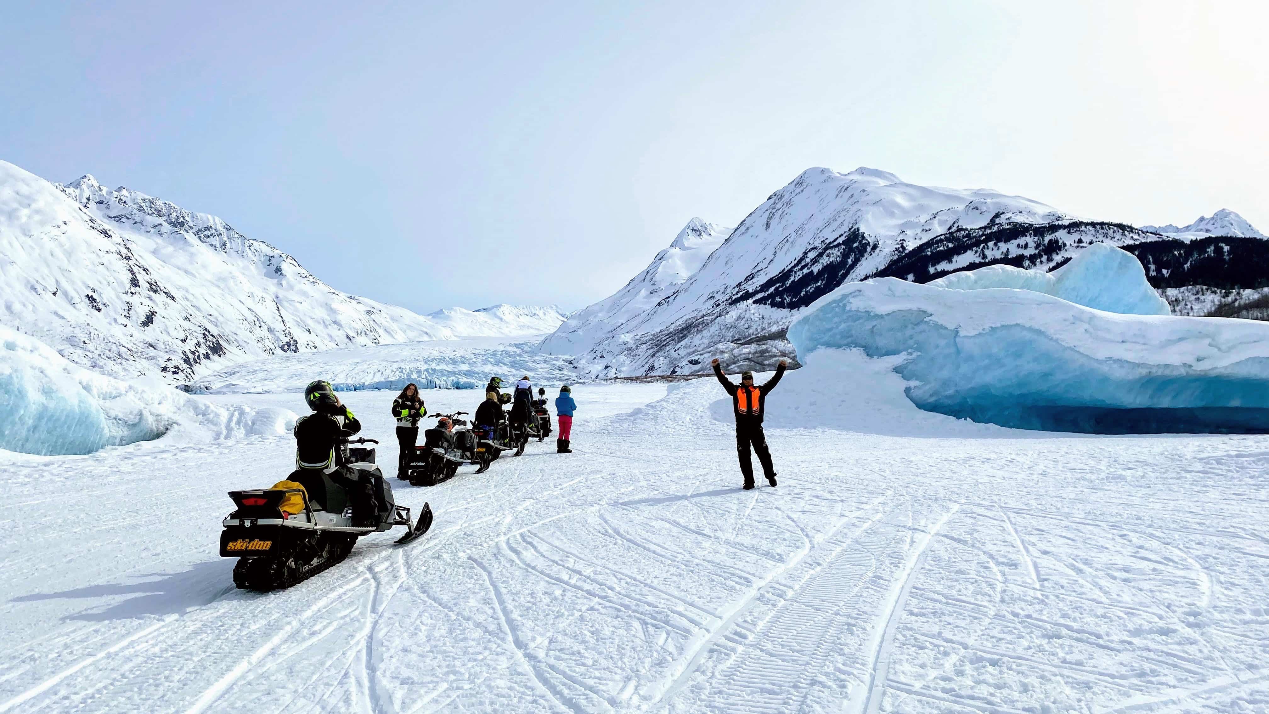 A man celebrating in front of a glacier with his snowmobile
