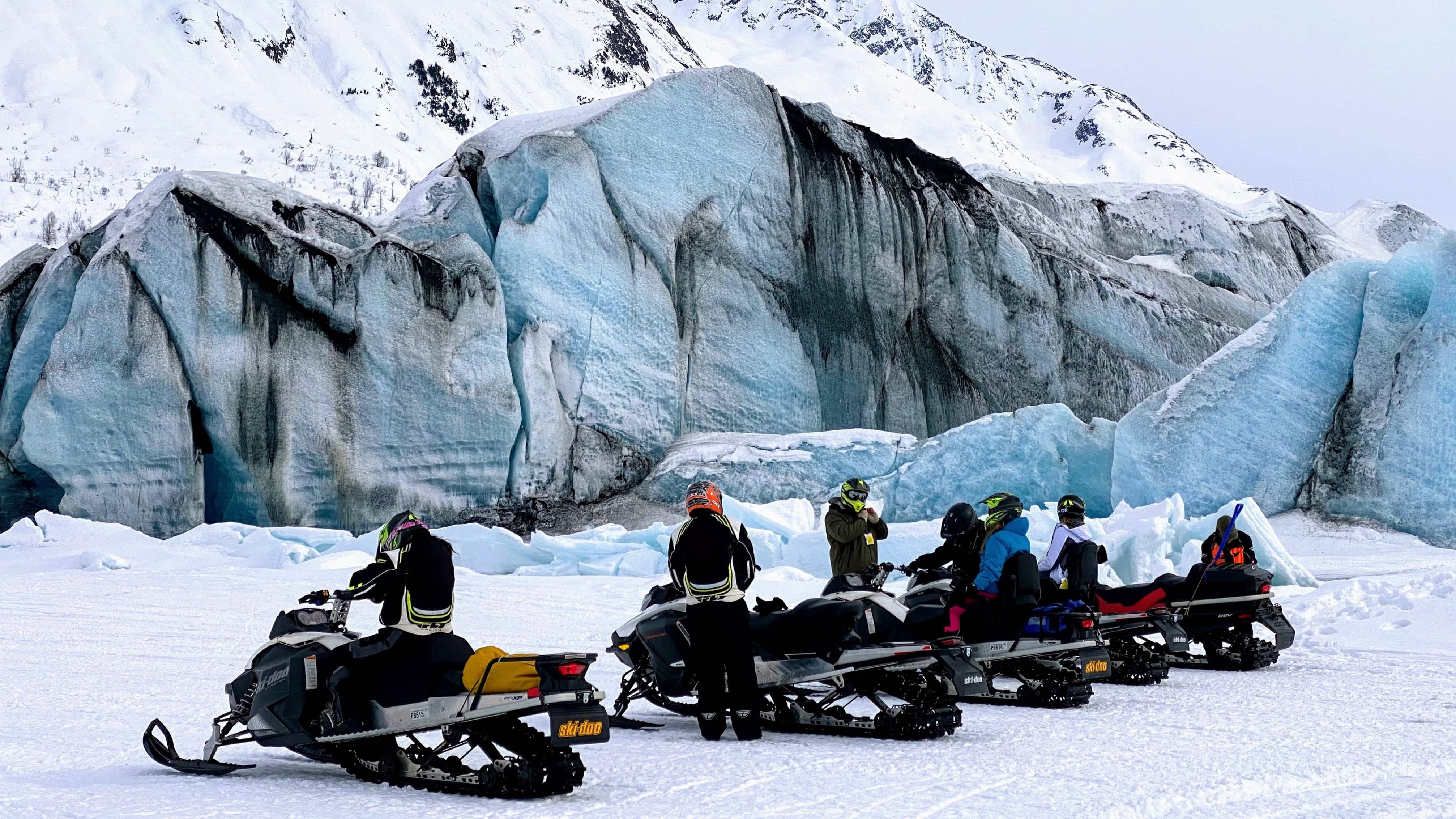 A crew of snowmobilers in front of a glacier
