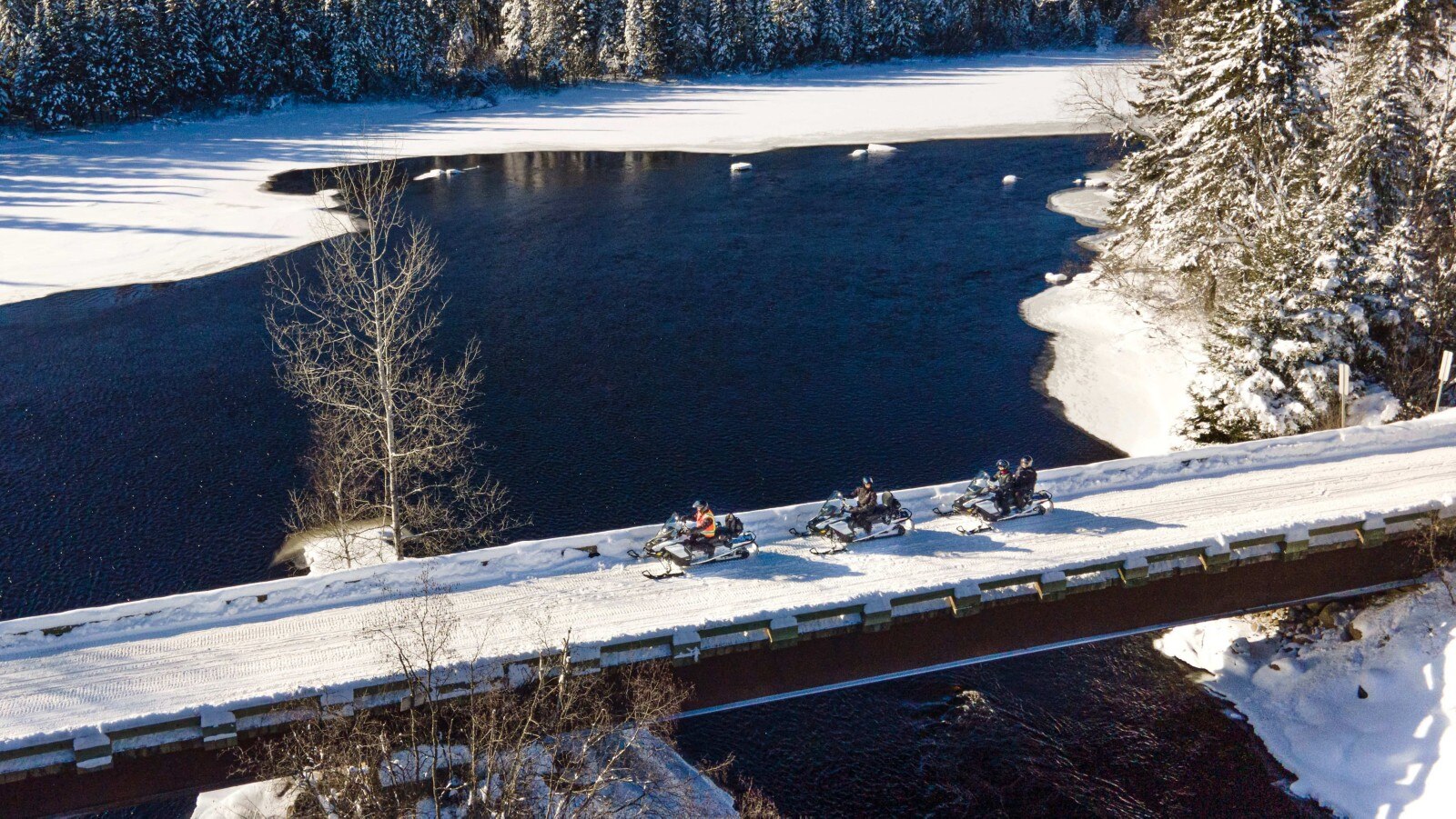 Snowmobiles crosing a bridge in winter
