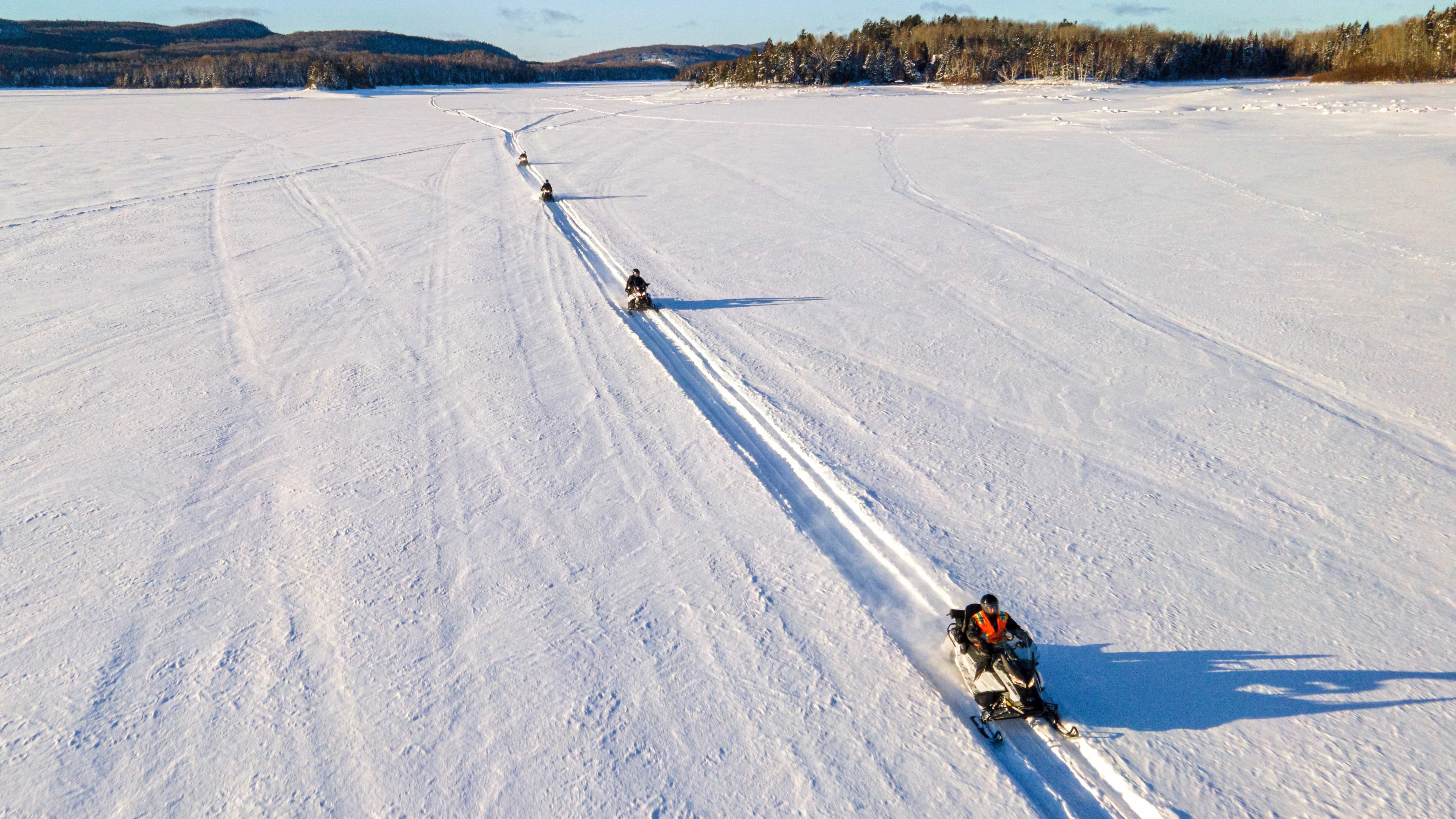 A group of snowmobilers crosing a frozen lake
