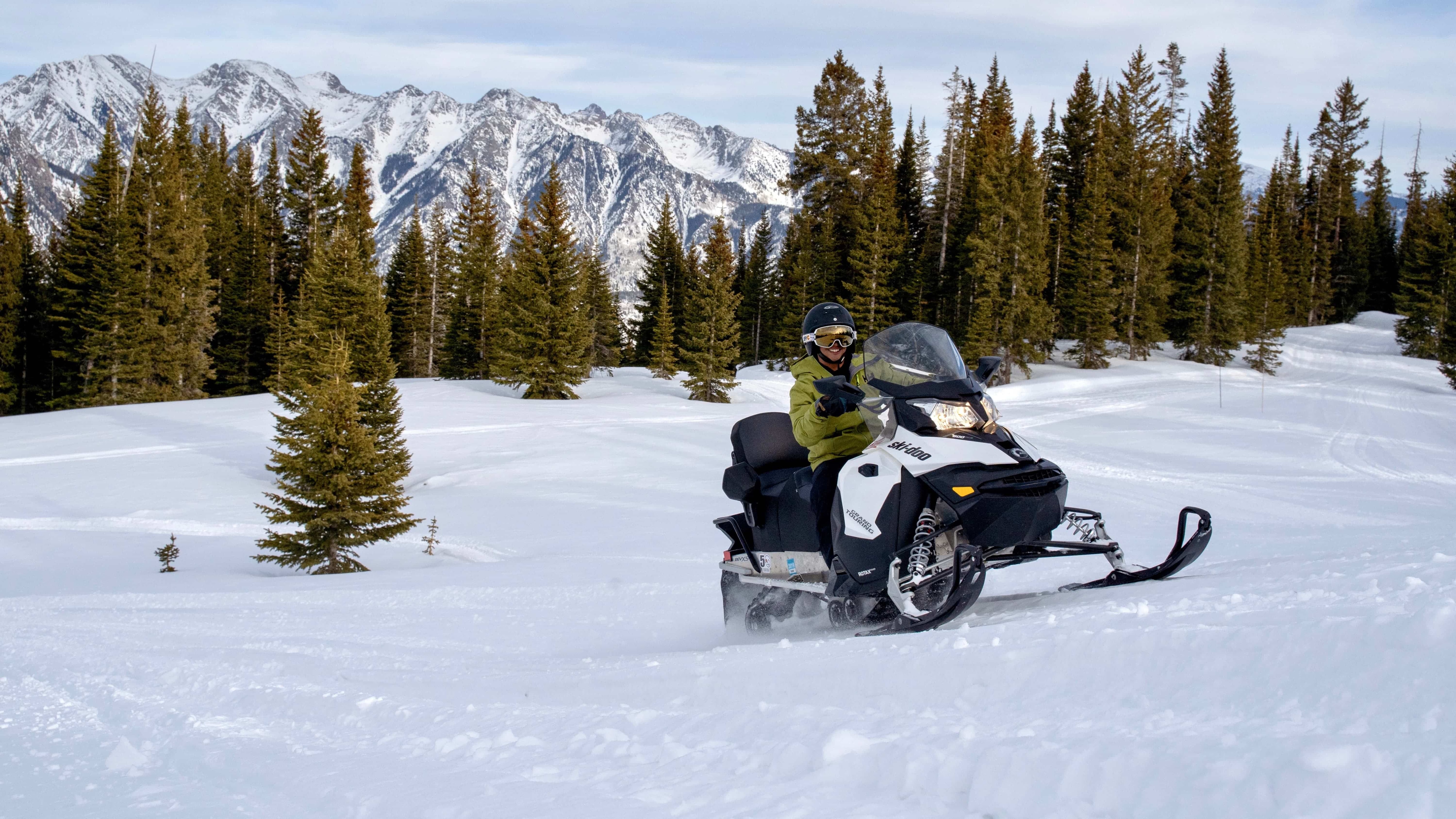 A person riding a snowmobile smiling through the snow 