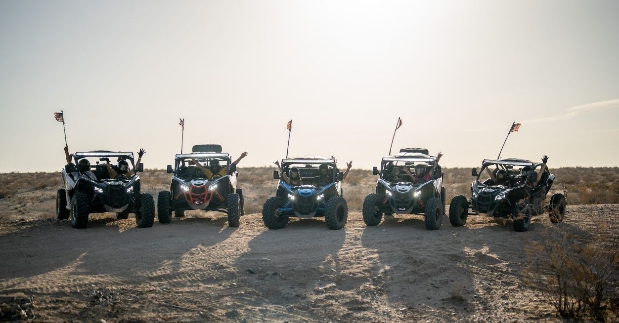 An image of 5 Can-Ams with riders in them, wearing helmets, with their hands up and American flags on top of the units.