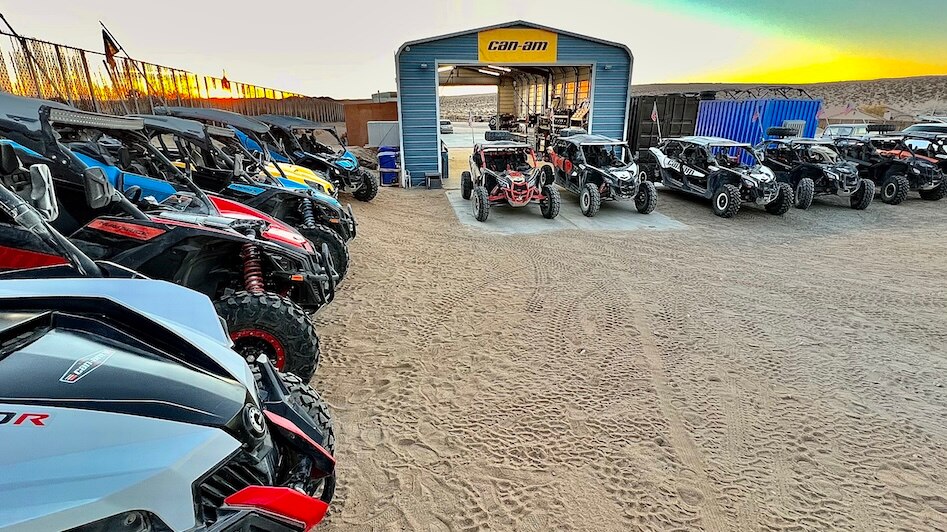 A group of Can-Am Off-Road units parked outside of a blue structure, with a yellow scene in the sky