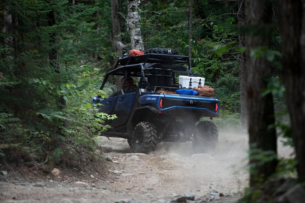 A blue Can-Am unit driving through the forest, with bags loaded onto it