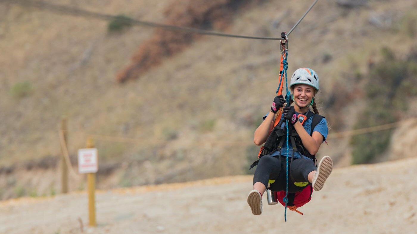 Female smiling on a zip line with a mountain in the back