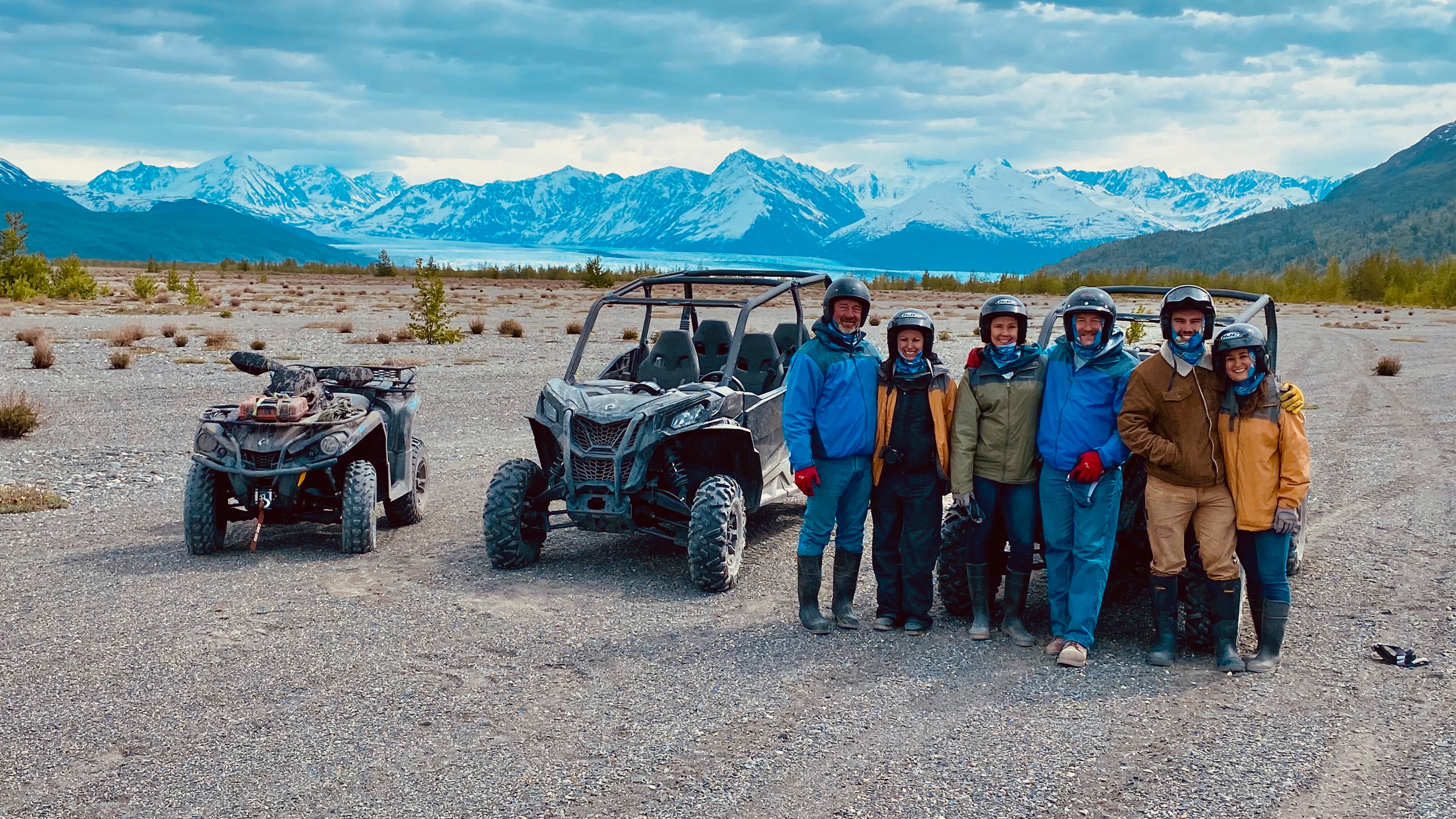 A group of people standing by a UTV and side by side in Alaska