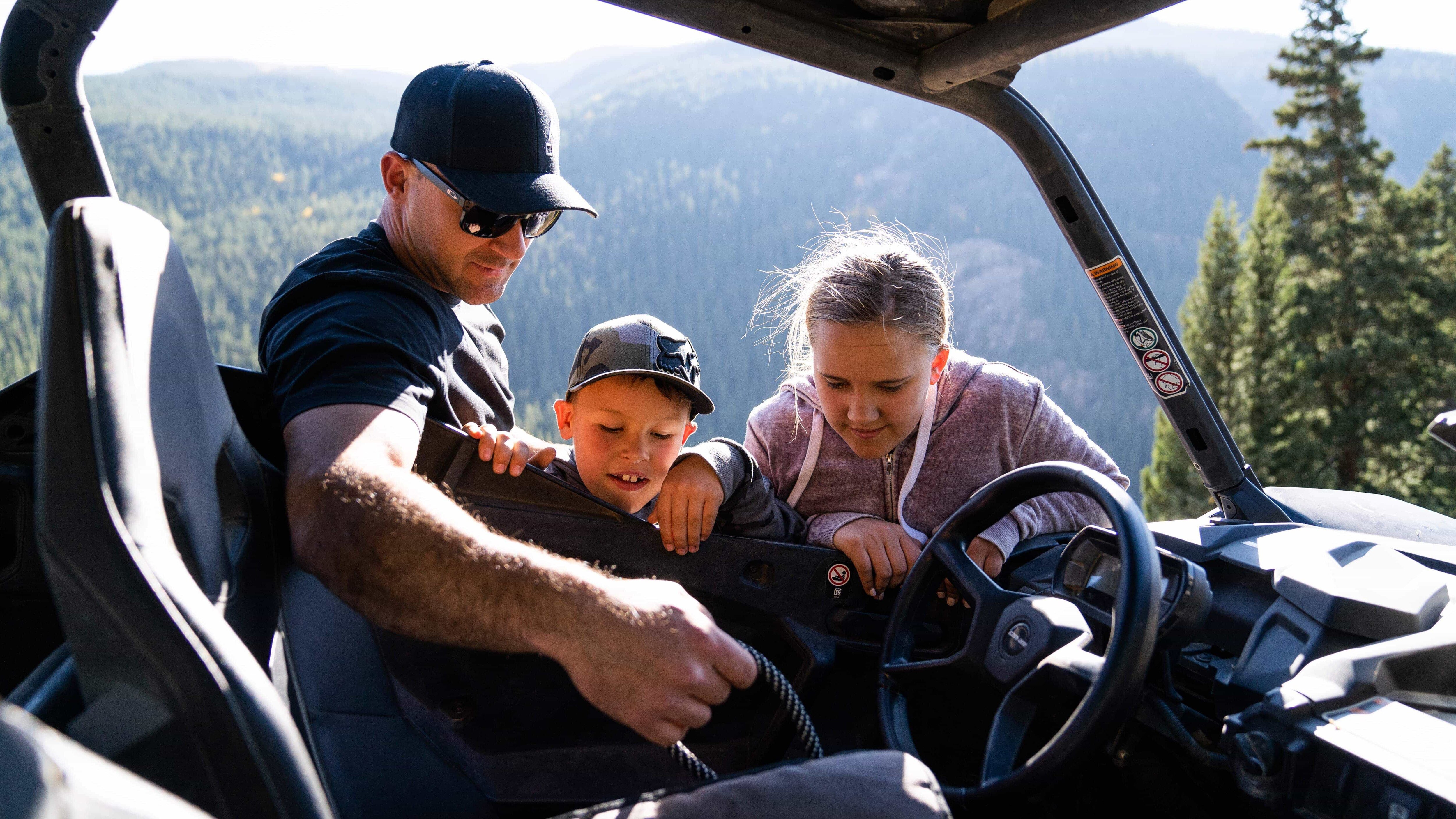 A man showing a girl and a boy how to open the door of an SSV