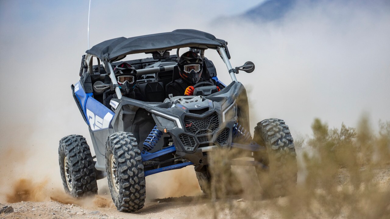 Two persons riding in a blue Can-Am Maverick