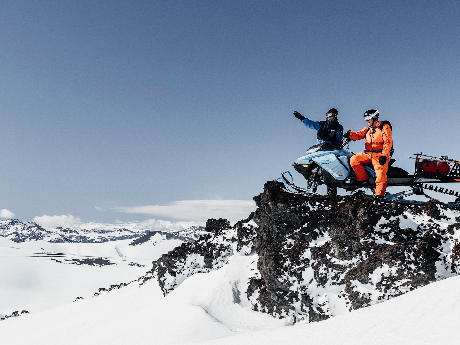 Two person on the edge of a cliff on a Ski-Doo