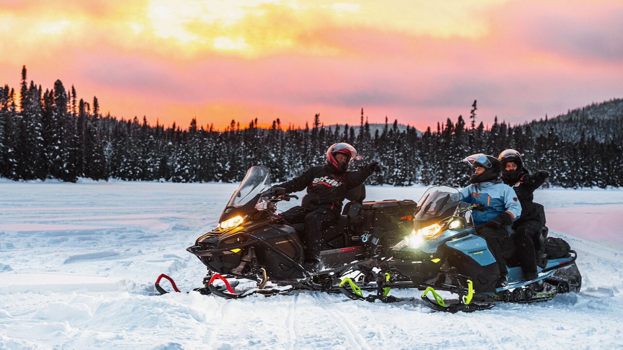 A family on snowmobiles with a sunset and a forest as background