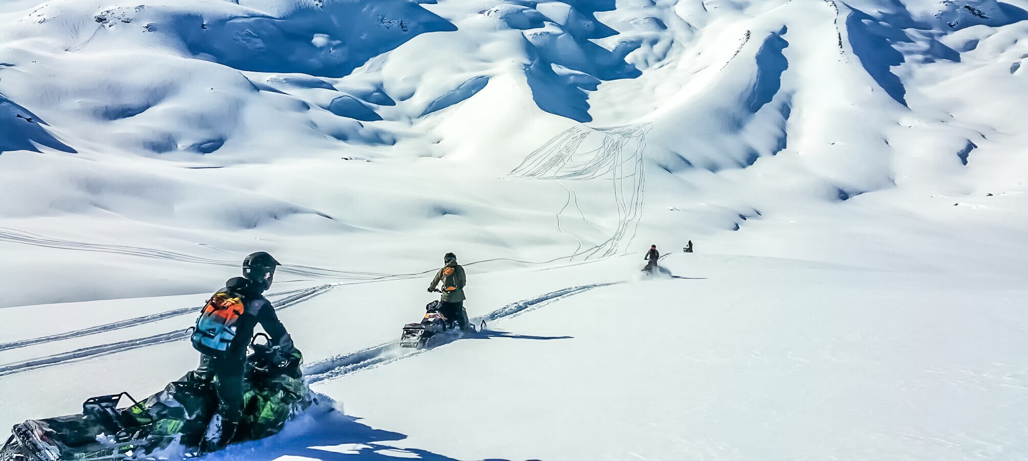 Group of snowmobilers driving in mountain's powder snow