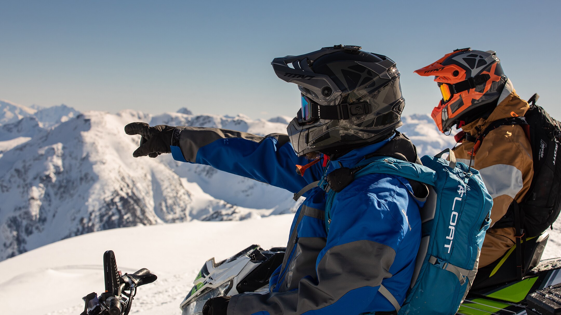 Group of persons at the top of a mountain with their snowmobiles and skis