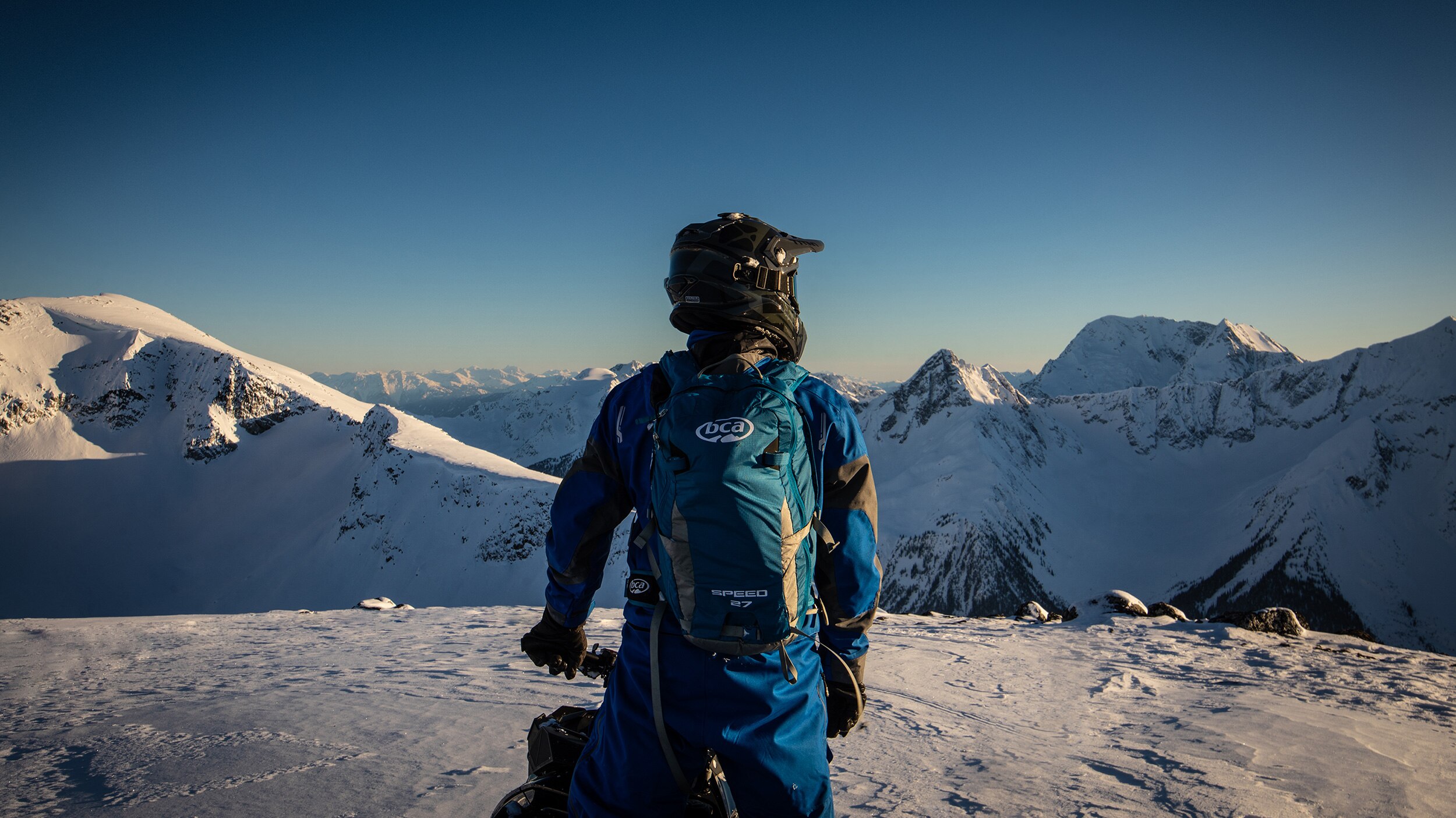 A snowmobiler contemplating the view at the top of a mountain
