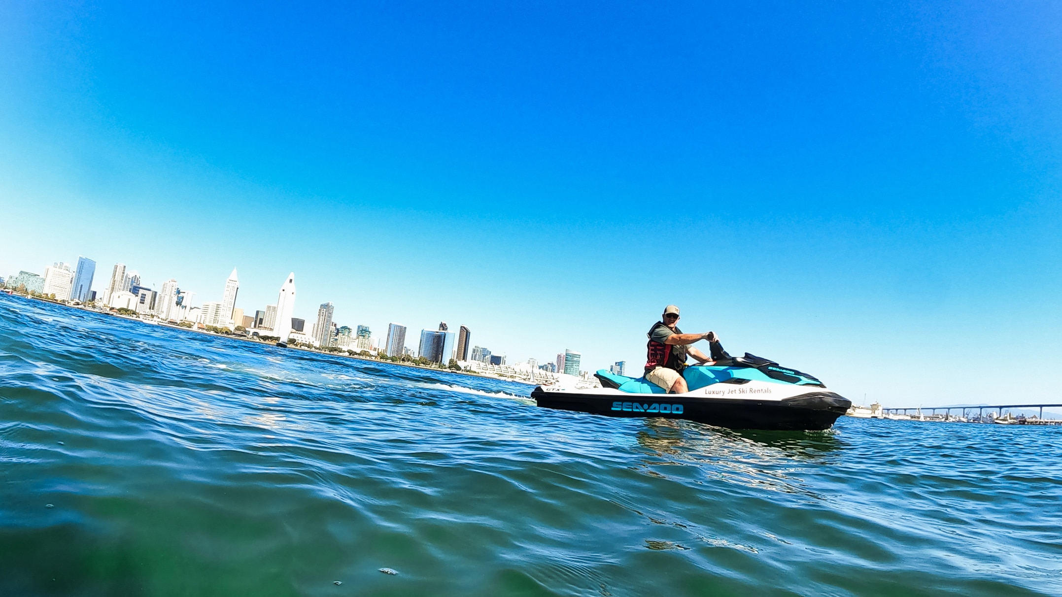 A man on a Sea-Doo in the middle of the water with a city in the background
