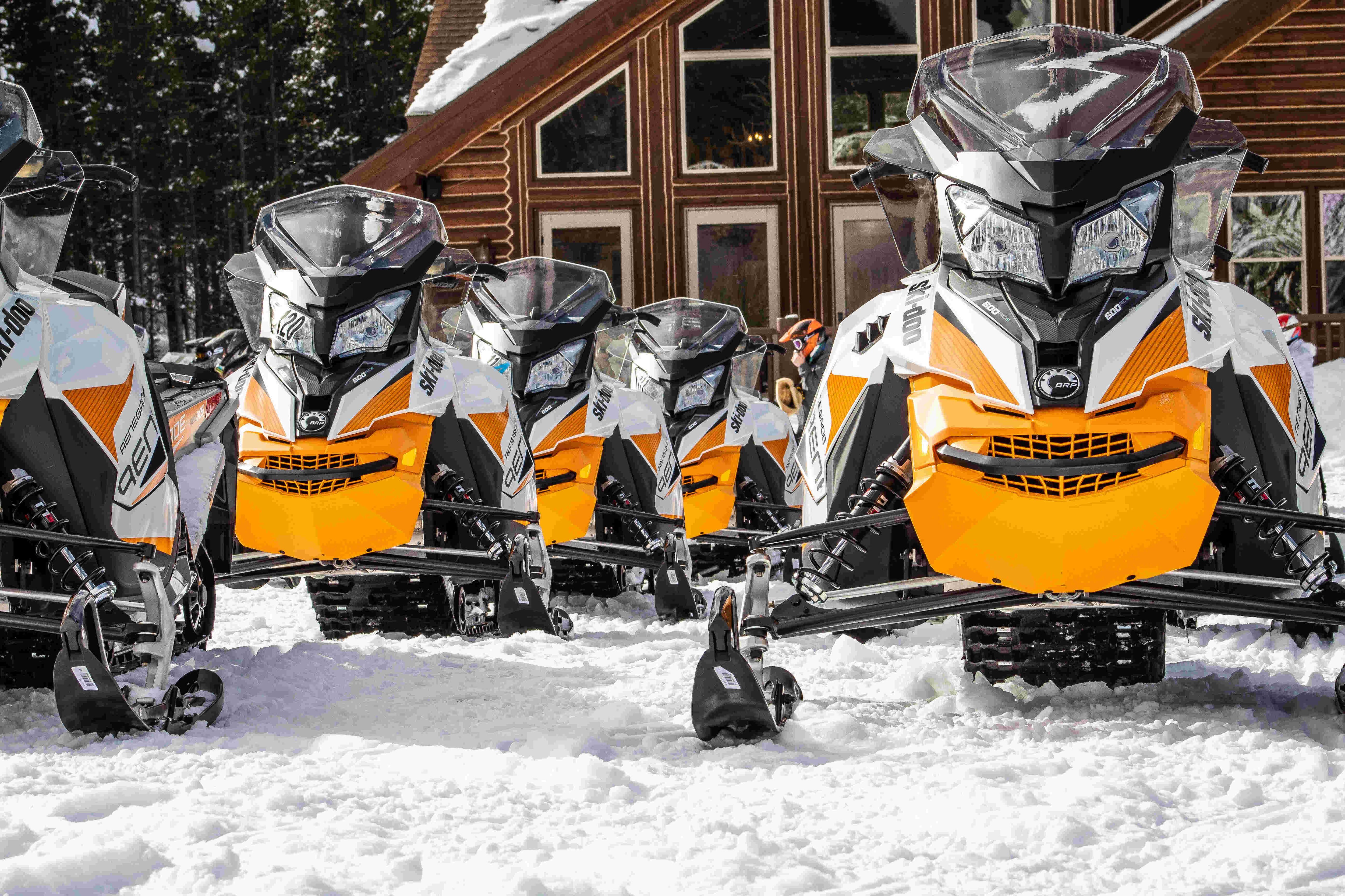 A line of Ski-doo's parked on the snow outside of a lodge cabin