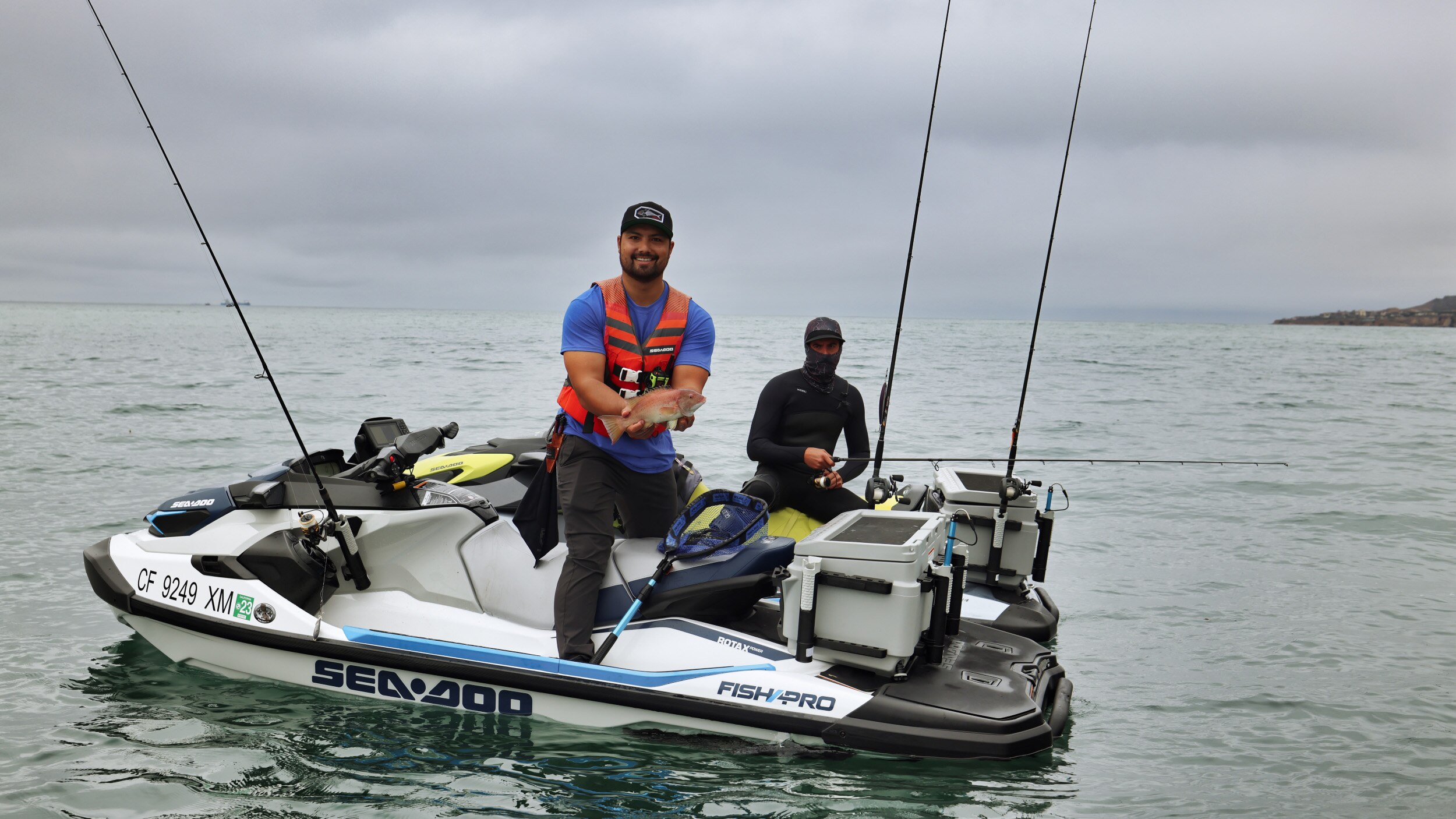 Two men on Sea-Doo Fish Pro's, one holding a caught fish 
