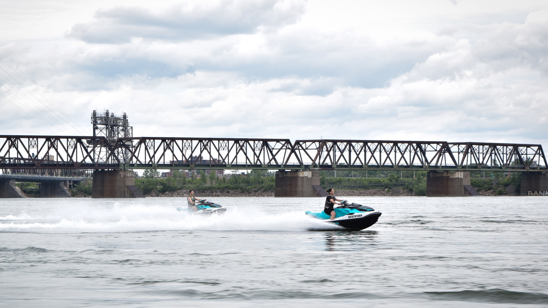 Deux personnes conduisant chacune une motomarine Sea-Doo à côté d'un pont